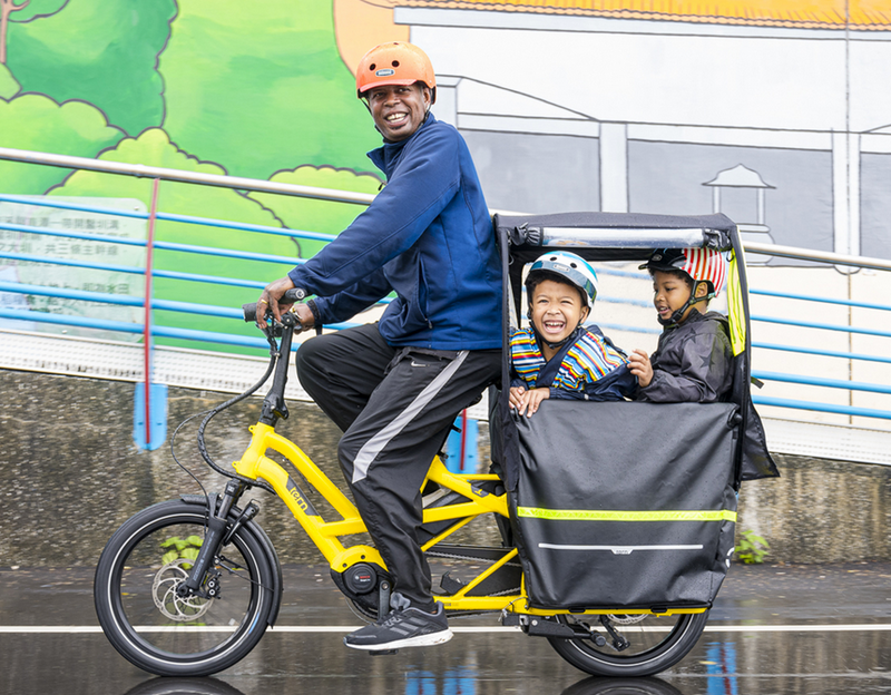 2 enfants protégés de la pluie transportés dans un vélo longtail Tern