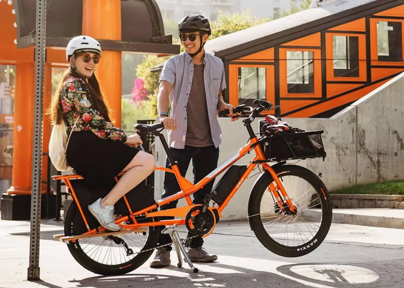 Le vélo longtail yuba kombi E5 orange peut transporter un adulte à l'arrière.
